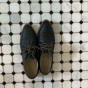 Lace up black matte loafers with dark wood sole.